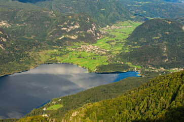 Aerial panoramic view of Bohinj Lake with mountain range and valley with small village. Scenic nature landscape during the autumn season. Travel and tourism concept. Triglav National Park, Slovenia