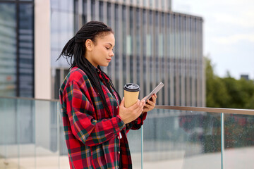 Focused African-American woman sipping coffee al fresco while diligently using a tablet.