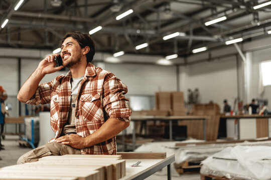 Young carpenter using his mobile phone in workshop - Powered by Adobe