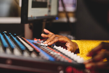 Crop ethnic female radio host using mixing console in studio
