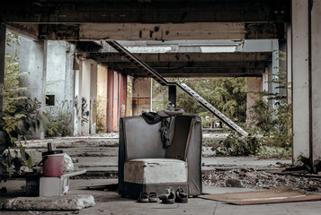The old black upholstered chair is in the middle of the abandoned buildings, it was left over...