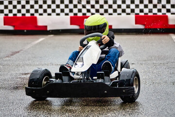 Obraz premium Young lover of extreme racing sports trains before a karting competition on the race track. Brave boy child racer in helmet driving children's electric karting