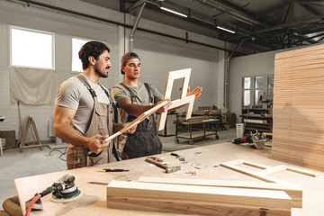 Two young men carpenters making furniture in warehouse of wood factory