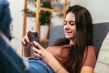 Beautiful teenager girl surfing social media on smart phone while having leisure time at her home.