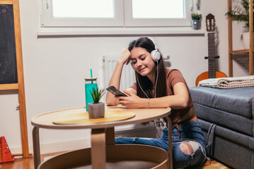 Beautiful teenager girl surfing social media on smart phone while having leisure time at her home.