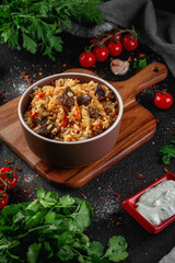 A bowl of pilaf on a dark table surrounded by vegetables and spices. Assorted Uzbek food set.