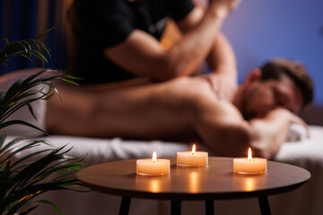 Handsome man having restorative back massage in spa salon, enjoying relaxing atmosphere, recharging after work. Masseuse gives therapeutic back massage to a visitor, the concept of healthy lifestyle.