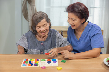 Caregiver and senior woman playing wooden shape puzzles game for dementia prevention