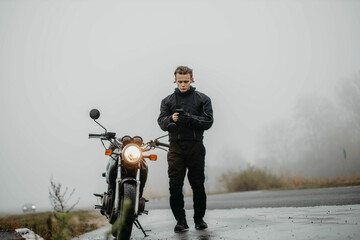 motorcyclist with a motorcycle in the rain and fog in autumn in cold weather.