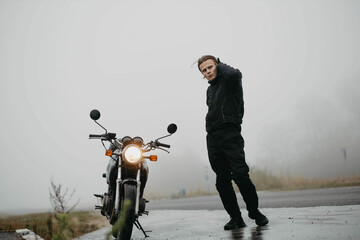 motorcyclist with a motorcycle in the rain and fog in autumn in cold weather.