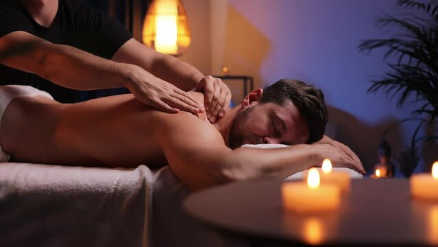 Handsome man having restorative back massage in spa salon, enjoying relaxing atmosphere, recharging after work. Masseuse gives therapeutic back massage to a visitor, the concept of healthy lifestyle.