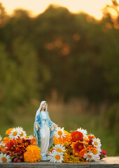 Statue of Our lady, grace virgin Mary with fresh flowers on natural blurred background. Blessed Virgin Mary, Mother of God. Symbol of Hope, Love, pray, Faith of God. Religion ritual, church holiday.