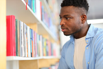 A focused young student in a library, engrossed in academic pursuits amidst shelves of books.