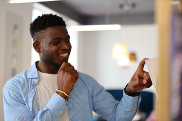 A cheerful young African American man in a bookstore, holding a book with a happy smile.