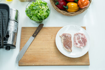 Top view wooden cutting board ,fresh pork,vegetable,tomato and a whisk on the kitchen on white table. Flat lay. Concept of food preparation, kitchen on background.