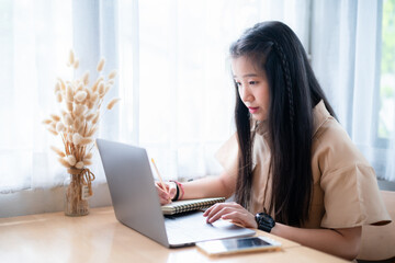 Happy of Young asian teen girl college student Taking written Notes to on notebook casual using laptop computer.Online education, elearning concept,freelance people businessfemale