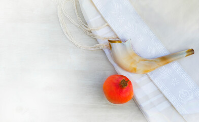 A shofar is placed on a tallit with a pomegranate on a white wooden surface. A symbol of the Rosh...