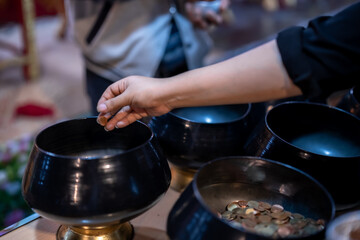 close up hand Asian woman tourist Make merit by dropping coins into the alms bowl. to Buddha for...