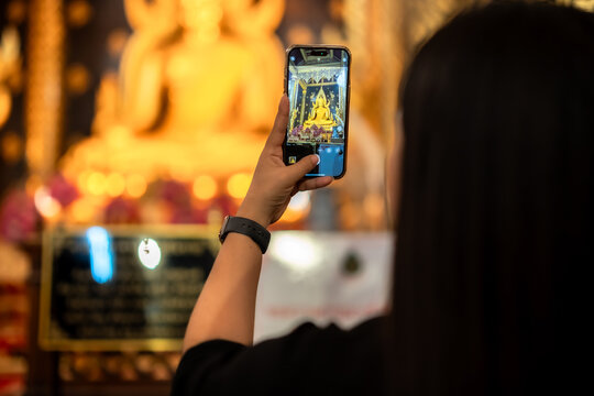 Asian woman tourist is taking picture by cell phone to Buddha for worship with faith to beautiful the golden Buddha images hall in the temple thailand belief in Buddhism.