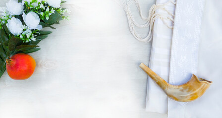 A shofar is placed on a tallit with a pomegranate, and flowers on a white surface. A symbol of the...