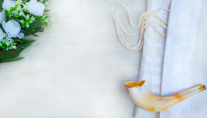 A shofar is placed on a tallit with flowers on a white wooden surface. A symbol of the Rosh...