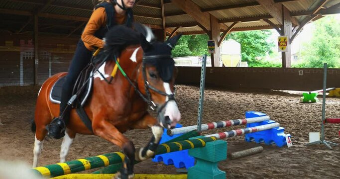 Young girl on her pony jumping obstacles in slow motion