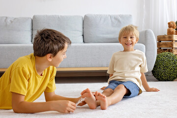 Happy positive children, tickling on the feet, having fun together, boy brothers at home having...