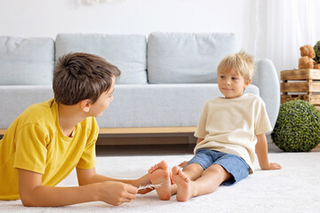 Happy positive children, tickling on the feet, having fun together, boy brothers at home having...