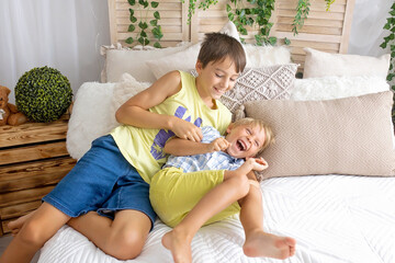 Happy positive children, tickling on the feet, having fun together, boy brothers at home having...