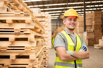 Portrait of warehouse worker checking stock of wooden pallets in storage warehouse.