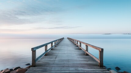 Fototapeta na wymiar A lone wooden pier stretching into the distance into calm water under muted sunrise and mist. 