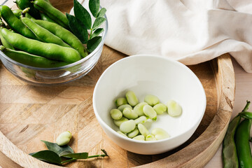 Bowl of green fava beans on a wooden tray.