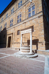 Pienza, Tuscany - Palazzo Piccolomini in piazza Pio II. In the foreground, the ancient stone and white marble well.