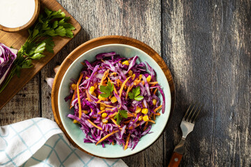 Vegan food concept, healthy food. Homemade purple cabbage salad with corn, carrots and greek yogurt on a rustic table. View from above. Copy space.