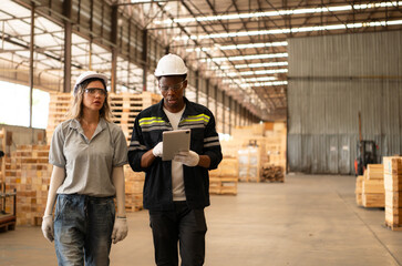 Front view of diverse female and male warehouse workers using digital tablet for working in wooden...