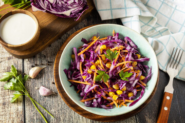Vegan food concept, healthy food. Homemade purple cabbage salad with corn, carrots and Greek yogurt on a rustic table.
