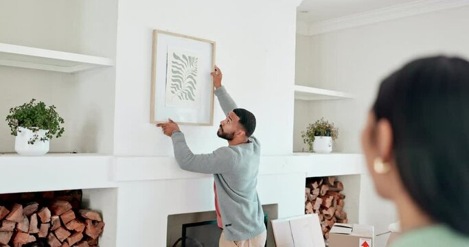 Picture, wall and a couple with help in a house for interior design, real estate or apartment furniture. Talking, living room and a woman speaking to a man about decoration of frame in a lounge