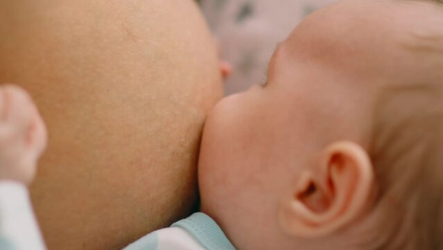 Infant sucks the mother's breast, close-up. Baby is resting and relaxing, enjoying sucking the mother's breast. Natural feeding of the child. Healthy food for a child. Motherhood and child care.
