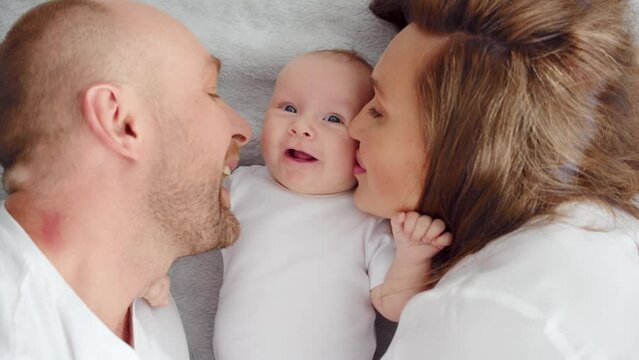 Close up Faces of the mother, father and infant baby. .Newborn baby with happy parents, top view. Happy family.  Healthy newborn baby in a white t-shirt with mom and dad. Cute  Infant boy and parents