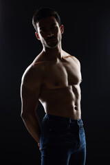 Bodybuilder man, topless and muscle in studio for wellness, healthy body and black background. Young guy, fitness and silhouette in jeans, portrait and strong for fashion, shadow or shirtless for art