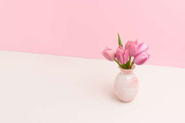 Vase with bouquet of tulip flowers in front of pink background. Copy space.