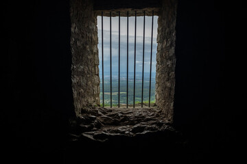 Aussicht auf Landschaft aus vergittertem Fenster in mittelalterlicher Burg mit sichtbarer Festungsmauer