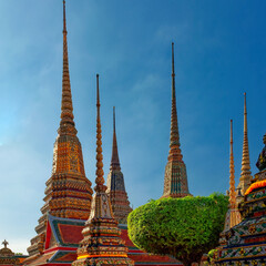 A Thai temple complex with ornate chedis decorated with gold and colorful tiles under a clear blue sky.