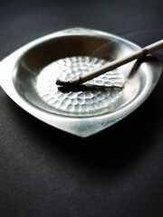 Silver ashtray and a thin cigarette on a black background.