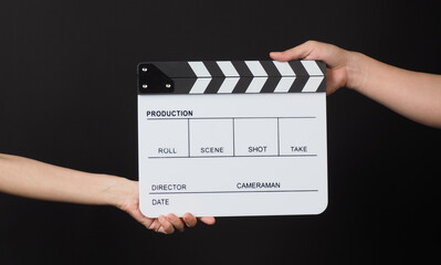 Hands send and hold Black clapper board or movie slate on black background.