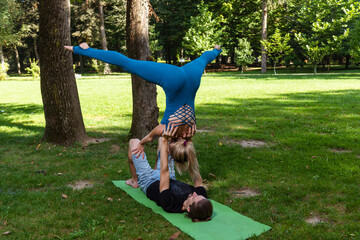 Boy and girl doing acro yoga outdoors in summer in public park