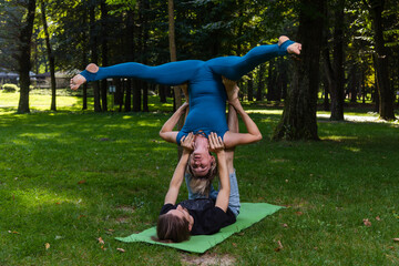 Boy and girl doing acro yoga outdoors in summer in public park