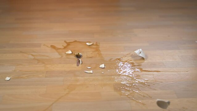 A cup of tea falls and breaks on the floor. Slow motion