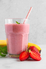 Strawberry and banana smoothie or milkshake in a glass with straw, fresh berries and mint on white...