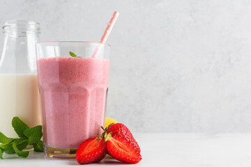 Strawberry and banana milkshake in a glass with a straw, fresh fruits and bottle of milk on white background